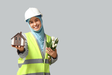 Muslim female construction worker with toy house and tulips on white background. Women's Day celebration