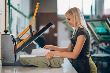 Side view of print shop worker using heating press on printed t-shirt.