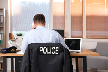 Male police officer working in office, back view