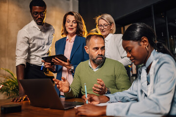 Interracial team with laptop at corporate office discussing strategy.