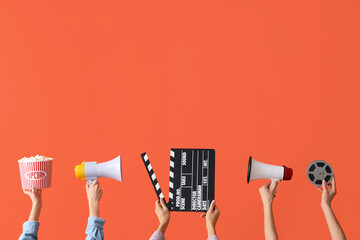 Many hands with bucket of popcorn, movie clapper and megaphones on orange background