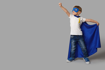 Cute little boy in superhero costume with yellow ribbon on grey background. International Childhood...