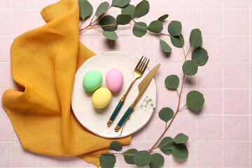 Beautiful festive table setting for Easter with colorful eggs and eucalyptus on pink tile background