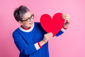 Photo of adorable cute senior woman wear trendy blue clothes look big large red paper card isolated on pink color background