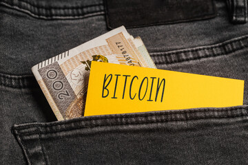 Yellow card with a handwritten inscription "Bitcoin", inserted into the pocket of gray pants jeasnow, next to Polish banknotes PLN (selective focus)
