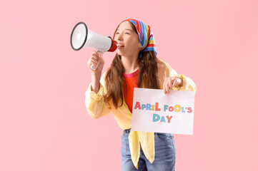 Funny little girl with card shouting into megaphone on pink background. April Fools' Day celebration