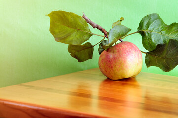Apple with a branch on a wooden table with a green background. Natural lighting. Place for text