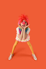 Funny girl with colorful wig and clown nose on orange background. April Fool's Day celebration