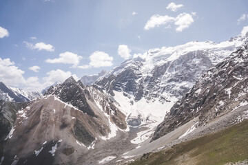 Panoramic landscape in the mountains with rocks and scree, with grass glades, snow and glaciers on a sunny summer day in the Fann Mountains in Tajikistan with mountain ranges