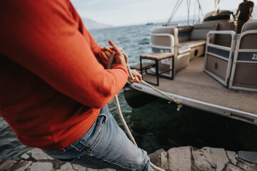 Close-up of a person's hands tying a rope while securing a boat to a dock, showcasing a nautical theme.