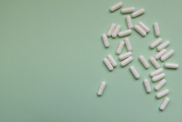 A bunch of white pills are scattered on a green background. The pills are small and white, and they...