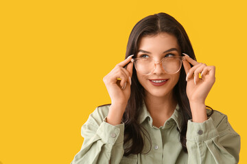 Happy smiling young woman in eyeglasses on yellow background
