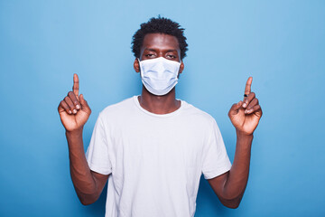 Portrait of black man wearing mask for coronavirus protection is pointing up with his two index...