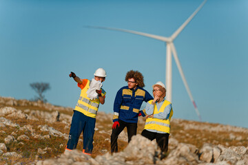 A team of engineers and workers oversees a wind turbine project at a modern wind farm, working...