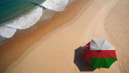 An aerial vista of a sandy beach with gentle ocean waves, featuring a beach umbrella adorned with the Oman flag. Ideal for Oman tourists seeking seaside relaxation