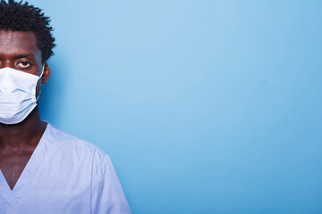 Close up of young man's eye while wearing a face mask for coronavirus protection. Face of black individual in scrubs with a mask for healthcare, standing against an isolated background.