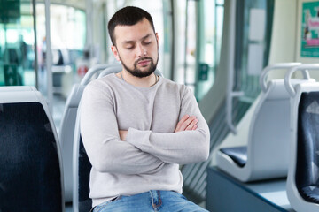 Young bearded guy sleeping while sitting with arms crossed on seat in tram on his way to work early in morning..