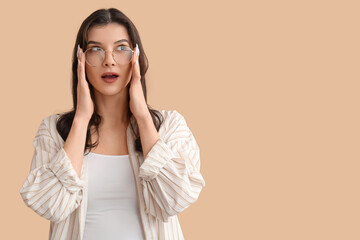 Surprised young woman in eyeglasses on beige background