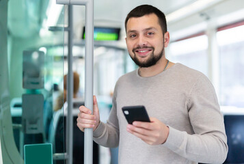 Portrait of positive bearded guy traveling in city bus and using mobile phone..