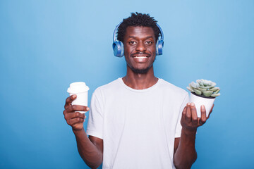 Portrait of happy African American man standing in front of a blue background with a potted plant...