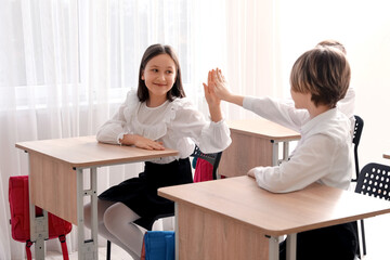 Cute children in school uniform giving high-five to each other in classroom