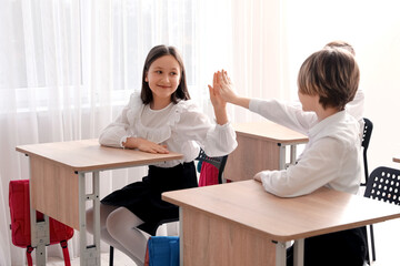 Fototapeta na wymiar Cute children in school uniform giving high-five to each other in classroom