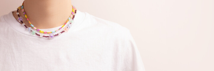 Banner with flower beads on a woman in a white t-shirt in front of beige background. Handmade accessory concept with copy space.