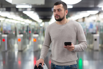 Young bearded man using his smartphone to check schedule while waiting for train on subway station platform ..