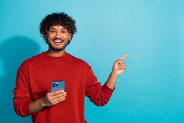 Photo of funny latin guy wearing red sweatshirt pointing finger empty space recommend mobile app...