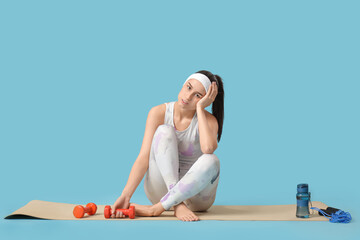 Sporty young woman tired after training with dumbbells on blue background