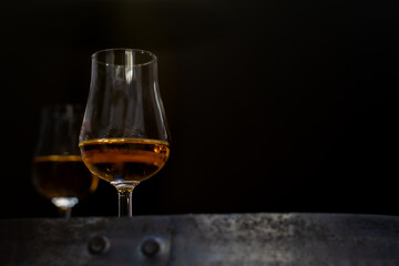 Whisky glass close-up on black blurred background on oak barrel