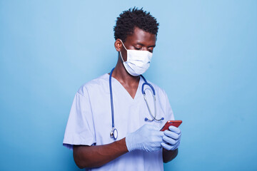 African american medical assistant in blue scrubs grasping smartphone in hand. Male healthcare...