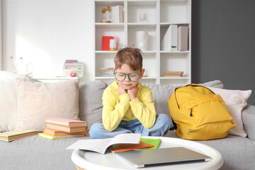 Cute little boy in eyeglasses doing homework at home