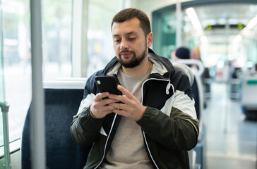 Portrait of european man standing in tram carriage and using his phone