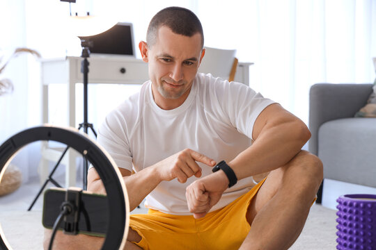 Male trainer with smartwatch recording sports video on phone at home