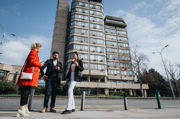 Young adults in professional attire having a conversation outside a modern office building, portraying a casual business atmosphere.