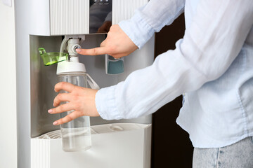 Woman filling bottle with filtered water from cooler in room