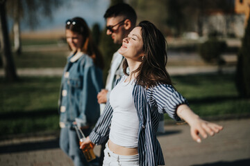 A happy young woman spreads her arms wide, embracing the warmth of a sunny day, accompanied by friends outdoors, evoking a sense of freedom and joy.