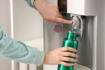 Female hands filling bottle with filtered water from cooler in room