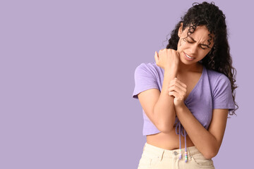 Young African-American woman with skin allergy scratching herself on lilac background
