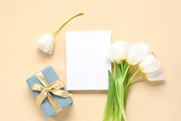 Blank card with beautiful white tulips and gift box on beige background. Mother's Day celebration