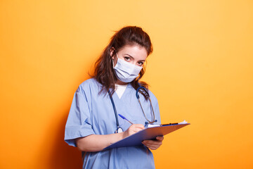 Woman doctor in blue scrubs taking notes on clipboard files, standing against isolated background....