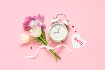 Card with word MOM, beautiful tulips and alarm clock on pink background. Mother's Day celebration