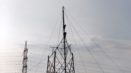 construction of a high voltage electricity tower, workers climb the tower to connect cables....