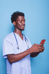 African American doctor in scrubs wears stethoscope and holds a smartphone, smiling confidently in...