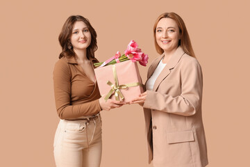 Beautiful mature woman and her daughter holding bouquet of tulips with gift box on brown background. Mother's Day celebration
