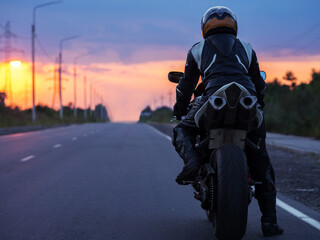 motorcyclist stands on an empty road at sunset , back view , copy space. Travel concept