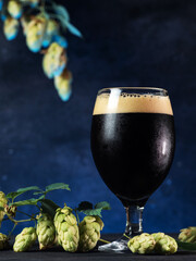 Glass of beer stout on a dark blue background, green hops