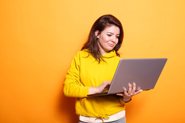 Naklejka premium In the studio, young adult looks at a laptop to use technology on camera. Portrait of a modern woman standing over an isolated background, holding a digital device and surfing the internet.