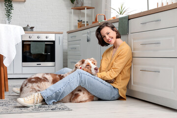 Pretty young woman sitting on floor with cute Australian Shepherd dog in kitchen
